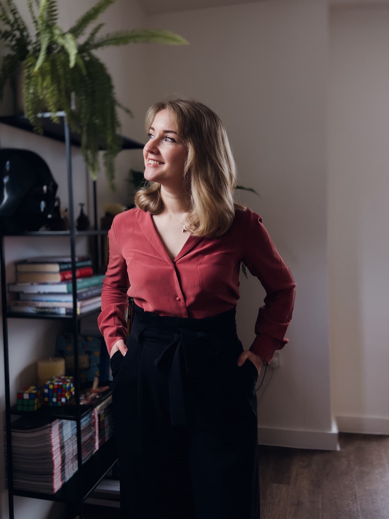 Anna standing by a bookshelf at home, looking towards the window